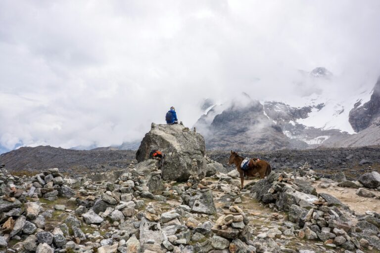 a man sitting on a rock with a donkey on the right on the Salkantay Route to Machu Picchu.