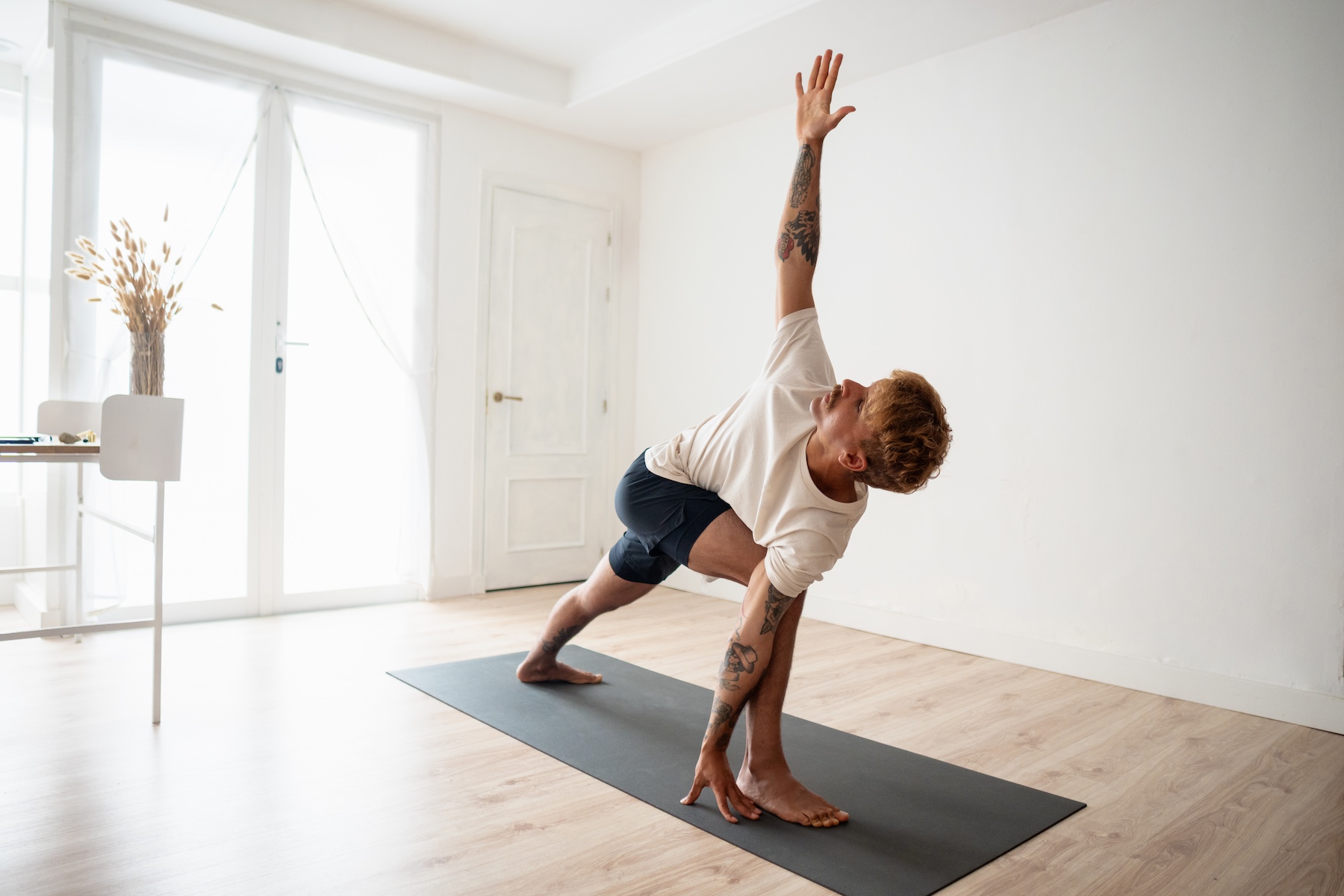 Man raising arm practicing Triangle pose yoga at home